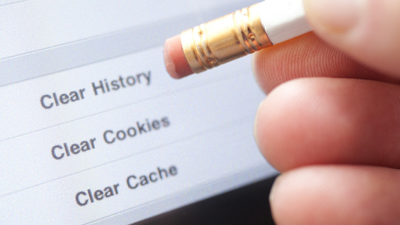 Person holding an eraser over a sheet that says Clear History, Clear Cookies, Clear Cache